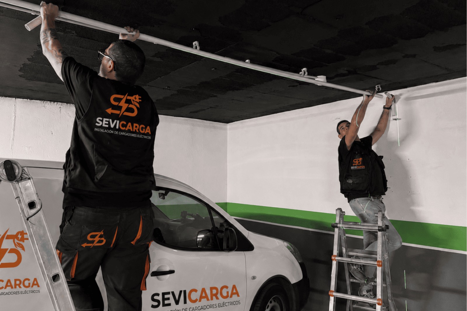 Equipo de instaladores de Sevicarga tendiendo la canalización de un punto de recarga en un garaje comunitario de Sevilla, con la furgoneta rotulada de la empresa